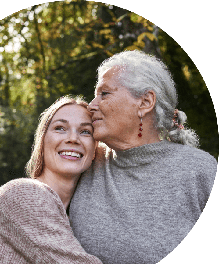 Adult daughter smiling and warmly embracing her elderly mother who lives with agitation in Alzheimer's dementia